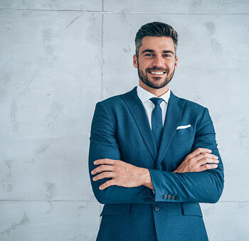 Portrait of handsome confident smiling businessman standing with arms crossed in the office and looking at camera.